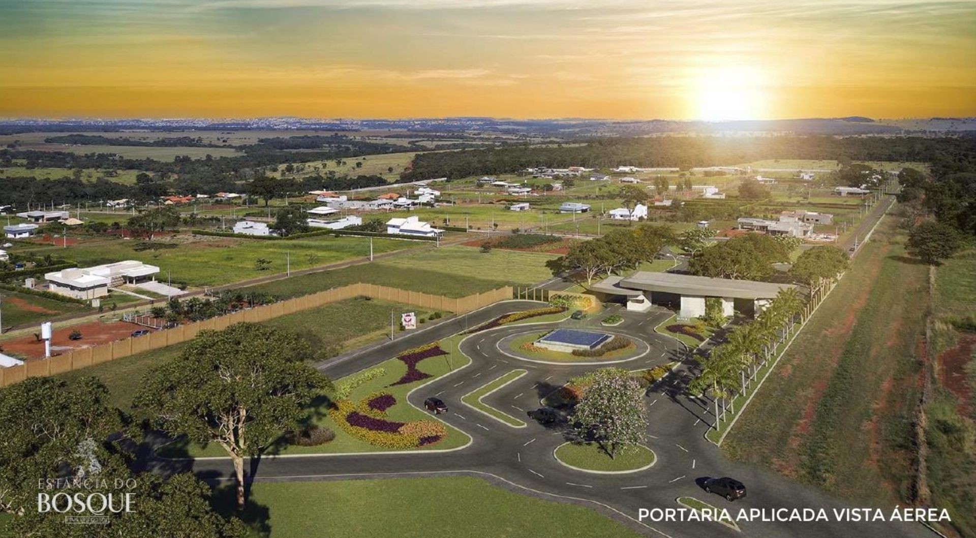 Aerial view of residential development with greenery, houses, and a gated entrance during sunset.