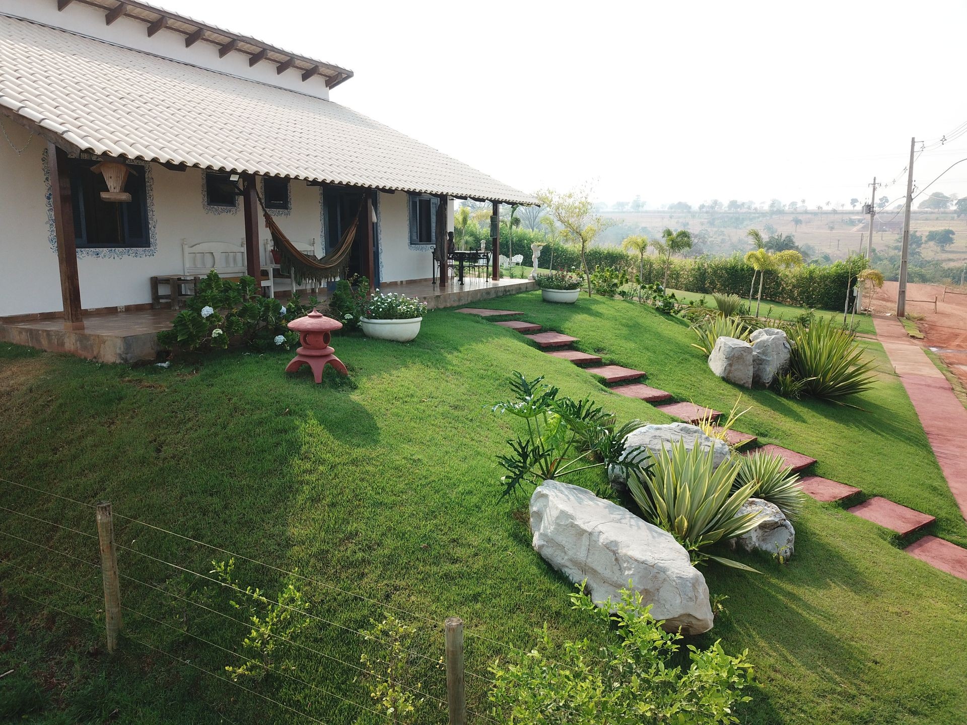 Charming house with a porch, hammock, and landscaped garden on a sunny day.