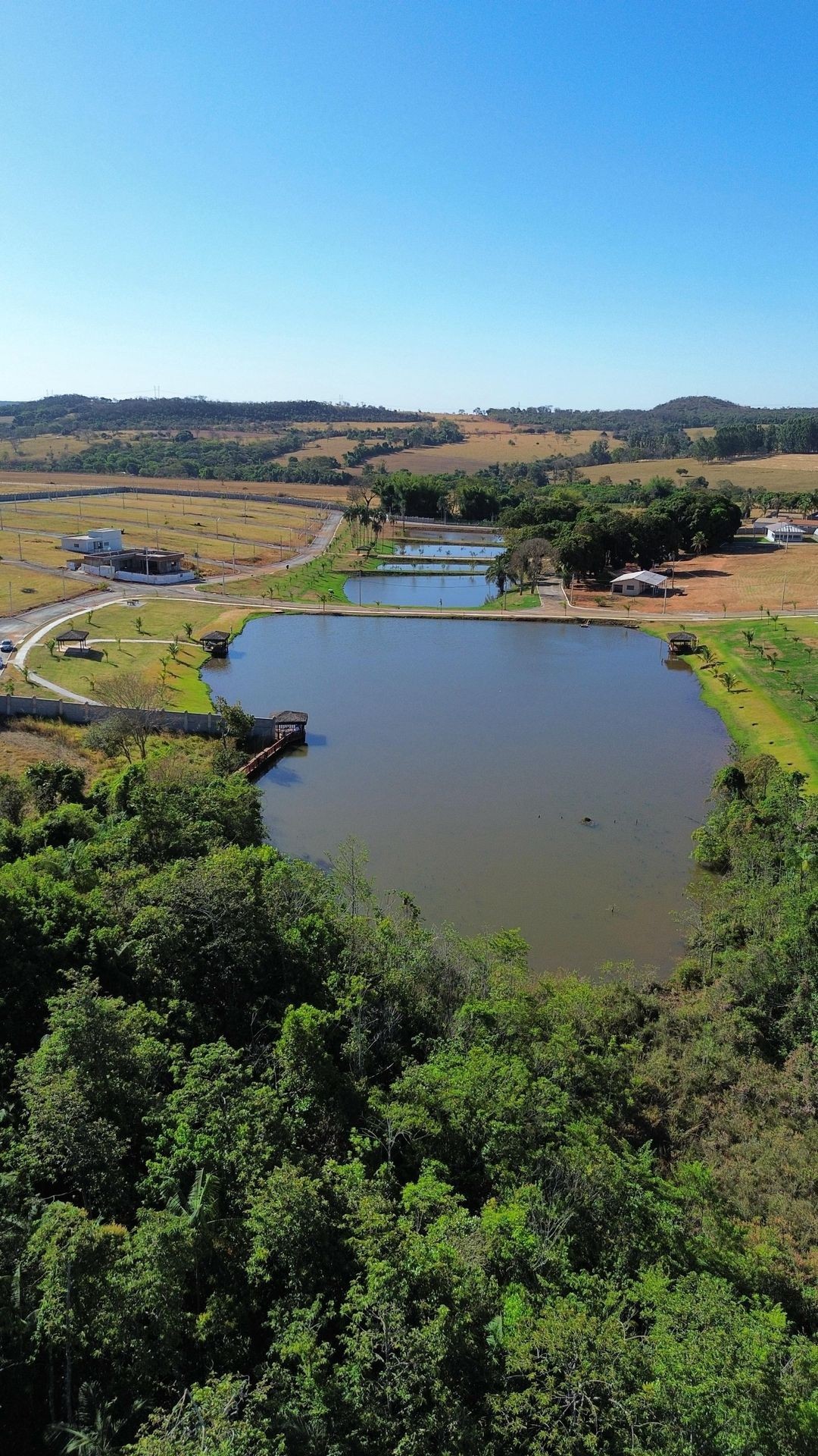 Aerial view of a large pond surrounded by greenery and fields under a clear blue sky.
