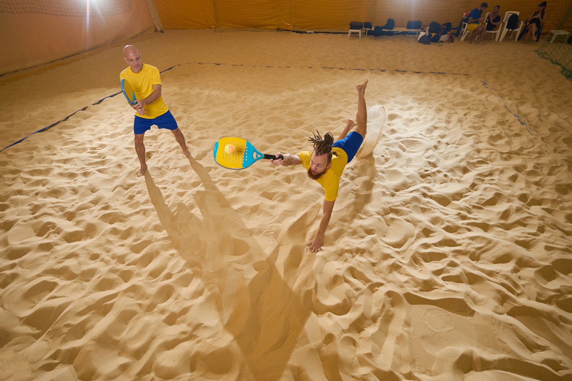 Dois companheiros de brincadeira estão pegando uma bola de tênis na areia